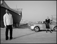 a man and woman standing next to a car on the beach