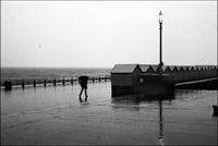 black and white photo of a person walking on a pier in the rain