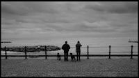 a black and white photo of a couple and their dogs looking at the ocean