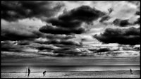 a black and white photo of people on the beach under a cloudy sky