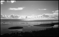 a black and white photo of a beach and clouds