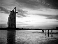 a black and white photo of people walking on the beach near the burj al arab